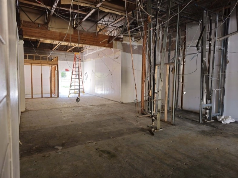 An unfinished commercial building interior with exposed wiring, framing, and a ladder during renovation.